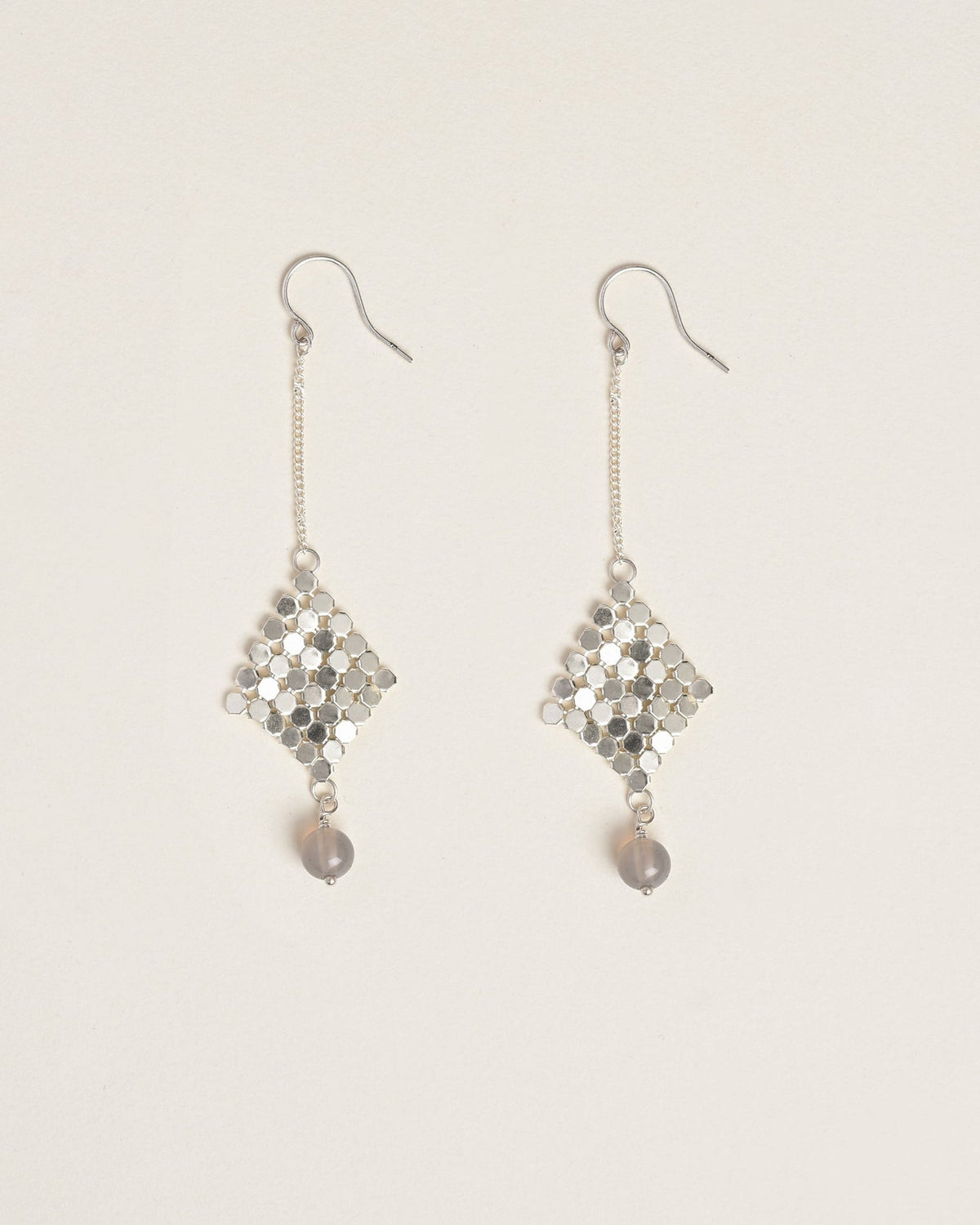 Pair of silver earrings with dangling elements on a light beige background